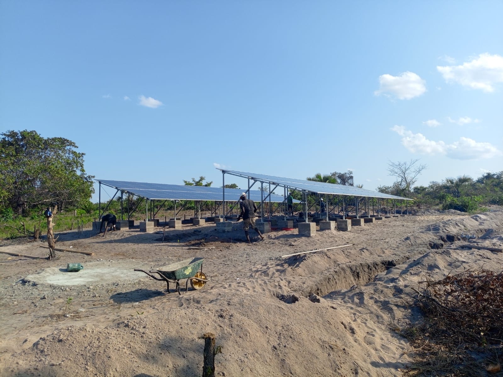 Solar panel array being installed on steel mounting frames at a rural site, with workers assembling the structure in sandy terrain.