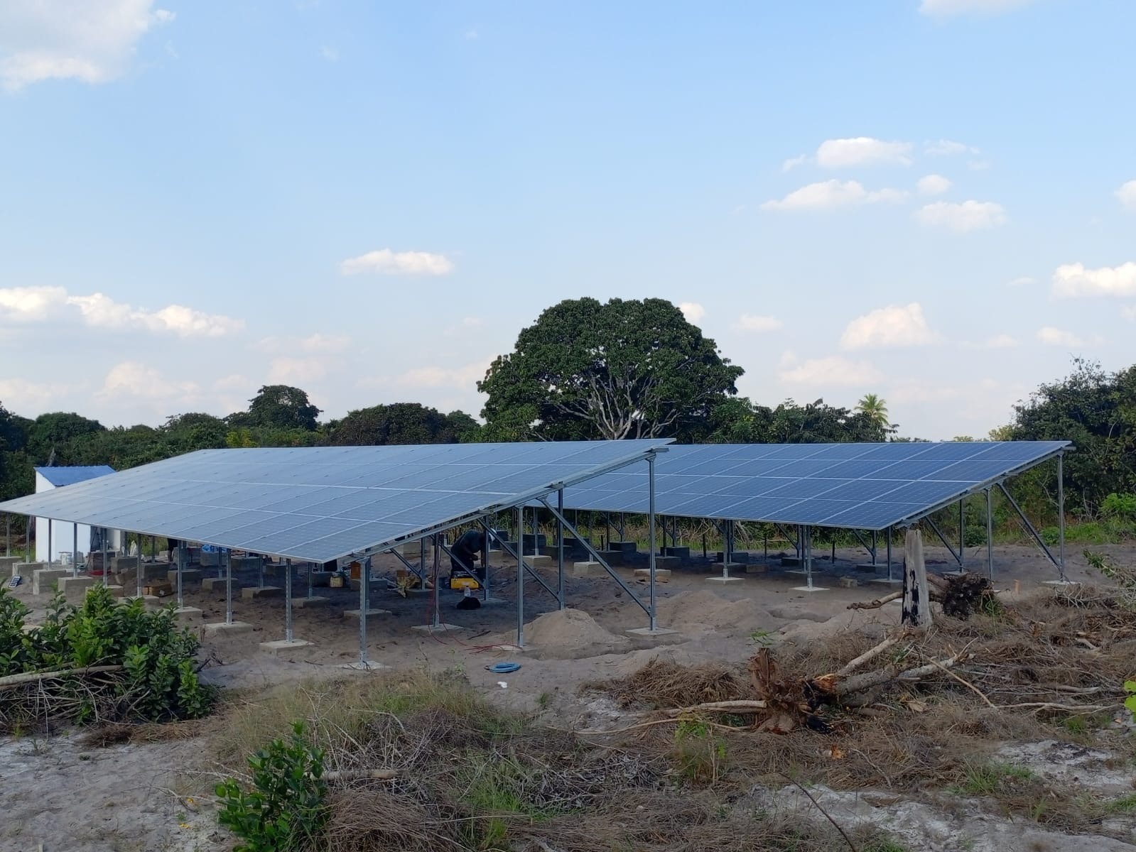 Completed rows of solar panels mounted on steel frames in a rural clearing surrounded by trees.